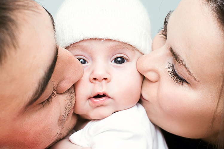 New parents on either side of baby, kissing baby on cheeks