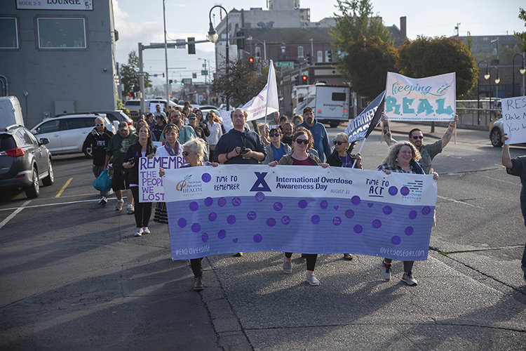 Dozens of people marching behind three people holding a banner to mark Overdose Awareness Day on August 31, 2023.