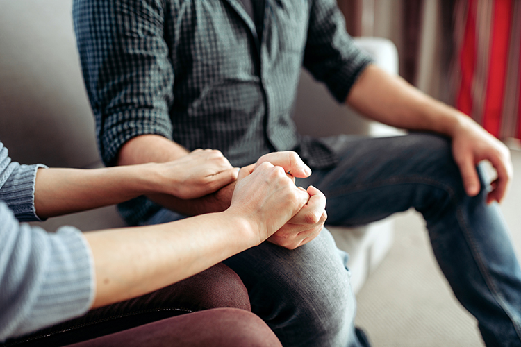 One person's hands reaching out and holding another person's hands in supportive gesture