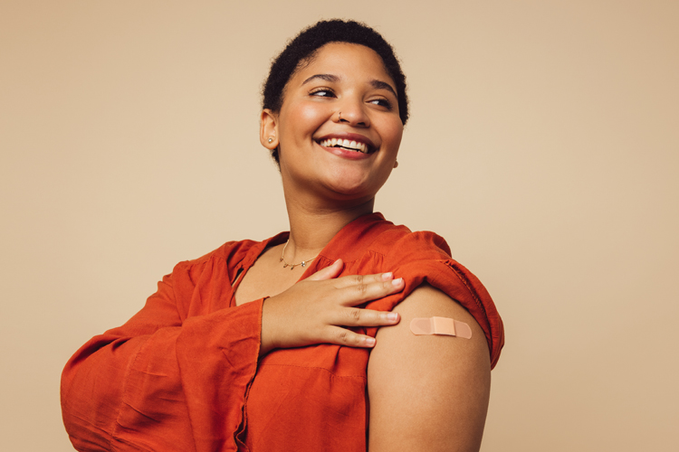 Smiling woman displaying bandage on shoulder from vaccination.