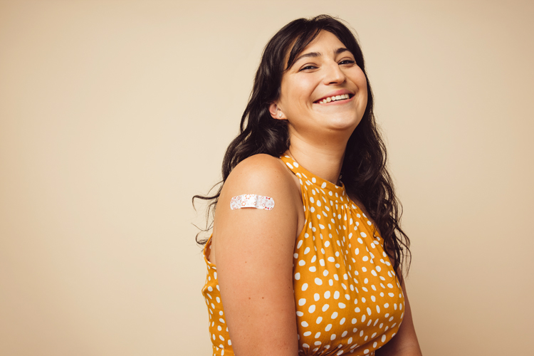 Woman smiling and displaying bandage on shoulder from vaccination.