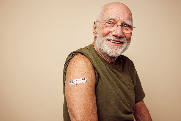 Man smiling and displaying bandage on shoulder from vaccination.