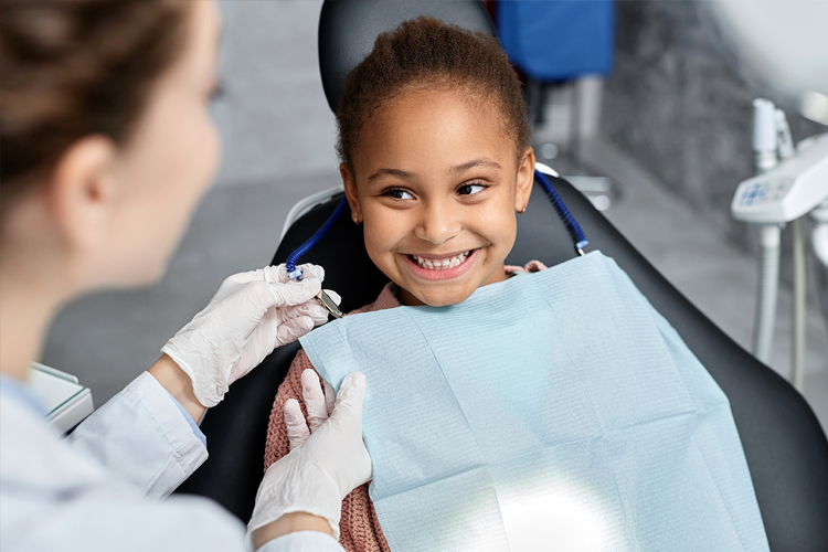 Smiling child at dental appointment with dental assistant clipping bib